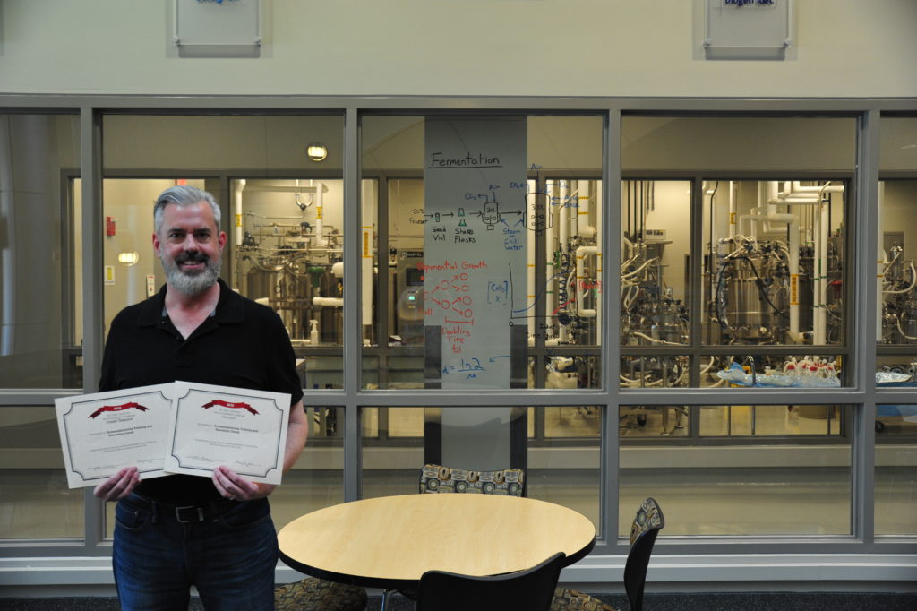 Brian Herring holds his web accessibility challenge certificate inside the lobby of BTEC.